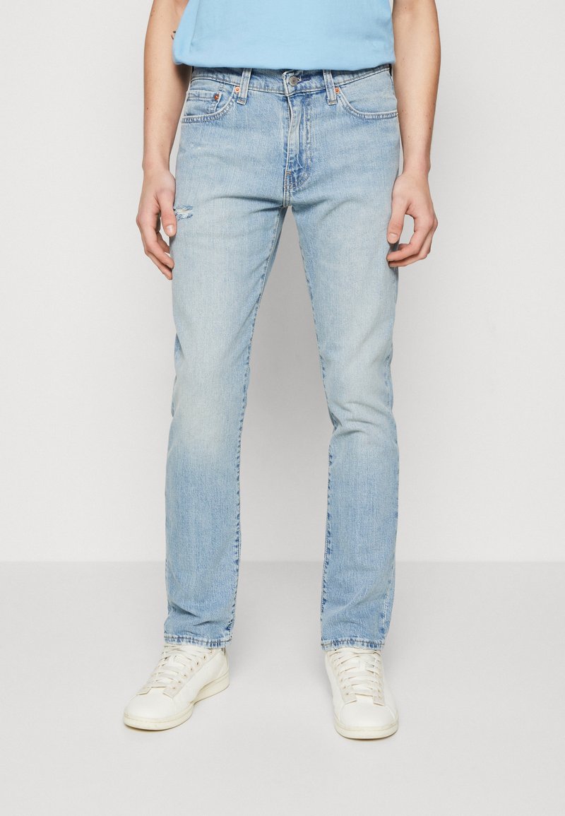 Jeans blu chiari con vestibilità dritta, leggera usura al ginocchio e design a cinque tasche, abbinati a sneaker bianche.