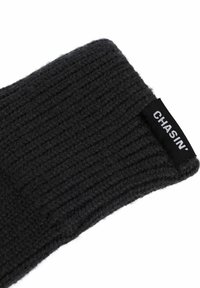 Črna pletena kapa z rebrasto teksturo in majhnim wovnim oznakam z napisom "CHASIN'" ob strani. Mehka in topla material.