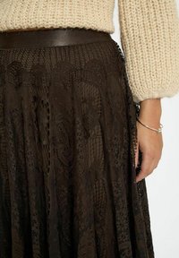Brun blonde nederdel med et tekstureret mønster, lagdelt design og en glat talje, suppleret med en strikket cremefarvet top.