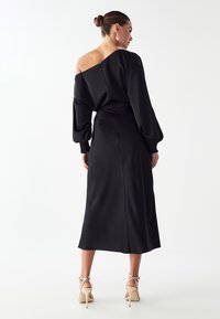 Čierne saténové šaty s off-the-shoulder dizajnom, dlhými puff rukávmi a priliehavým pásom. Hladká textúra s dĺžkou do polovice lýtok.