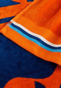 Toalla naranja con un diseño de flores audaz, sobre un fondo azul y un dobladillo decorado con rayas naranjas, blancas y azules. Textura suave.