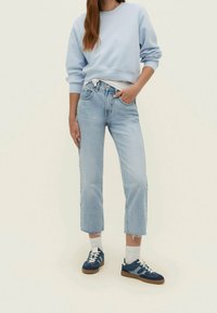 Sudadera de algodón azul claro con puños acanalados, combinada con jeans de tiro alto y cortos de lavado claro. Zapatillas oscuras con detalles blancos.