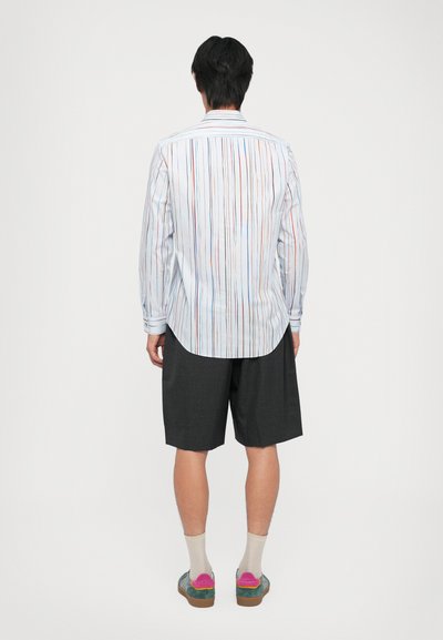 Chemise à manches longues rayée avec des rayures verticales multicolores, en tissu bleu clair, avec un ourlet arrondi, assortie à un short gris et des chaussures colorées.