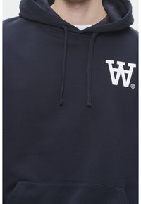 Marineblauer Hoodie aus einer Baumwollmischung mit einer vorderen Bauchtasche und einem weißen Logo auf der linken Brust. Mit Kapuze und Kordelzug ausgestattet.