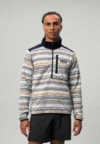 Többszínű mintájú fleece pulóver, geometrikus formákkal. A szabása puha, álló gallérral és cipzáras zsebbel a mellrészén.