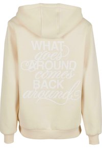 Krämfärgad hoodie i mjukt material med en känguruficka. Har stor vit text på baksidan: "DET SOM GÅR RUNDT KOMMER TILLBAKA."
