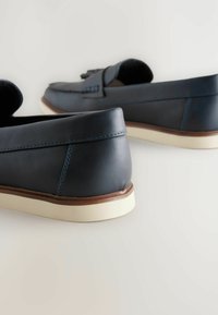 Zapatos de piel azul oscuro de tipo slip-on con una textura suave, que presentan un acento de costura en contraste y una suela de goma blanca.
