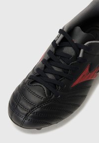 Sorte fotballsko i skinn med teksturerte overflater, røde detaljer og svarte lisser. Rund tådesign og lav krage.