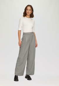 Lichtgrijze wijde broek met een hoge taille en plooien aan de voorkant, van een gladde stof; gecombineerd met een aansluitend wit T-shirt met korte mouwen en zwarte schoenen.