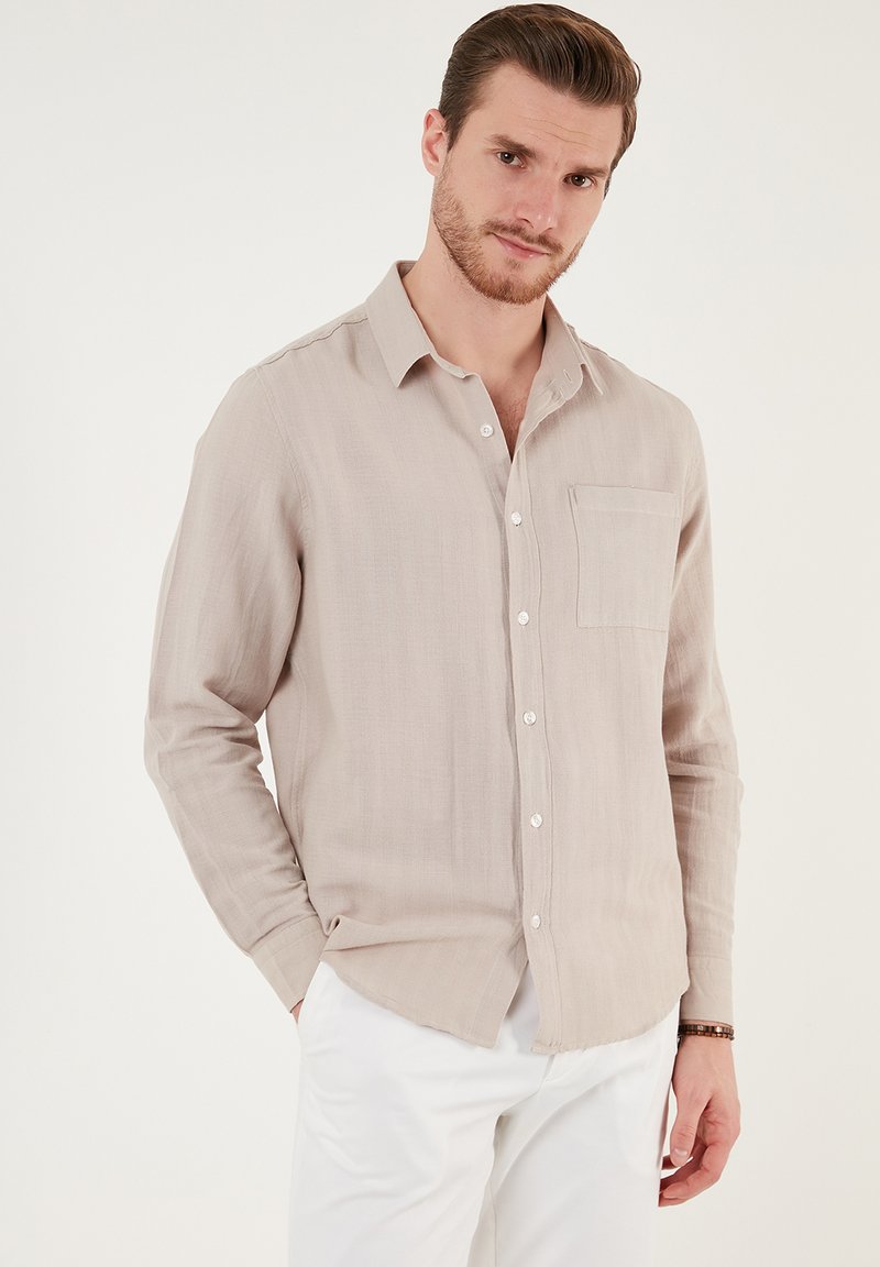 Beige Hemd mit Knöpfen aus einem strukturierten Stoff, ausgestattet mit einer Brusttasche, langen Ärmeln und einem klassischen Kragen. Schlichte Gestaltung.