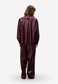 Bordeaux faux leren outfit met een losvallend jasje en broek met wijd uitlopende pijpen, met een gladde textuur en een minimalistisch ontwerp.
