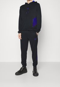 Svart hoodie och joggingbyxor set med blåa randiga detaljer, logotyp på bröstet och låret, strukturerad tyg och justerbar dragsko på huvan.