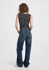 Black and white striped sleeveless top paired with high-waisted, loose blue denim jeans. Curly hair visible from the back.