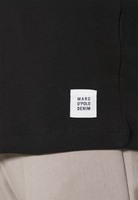 Zwarte T-shirt van katoen met een gladde textuur; heeft een wit merkembleem met de tekst "MARC O'POLO DENIM" gestikt op de zoom.