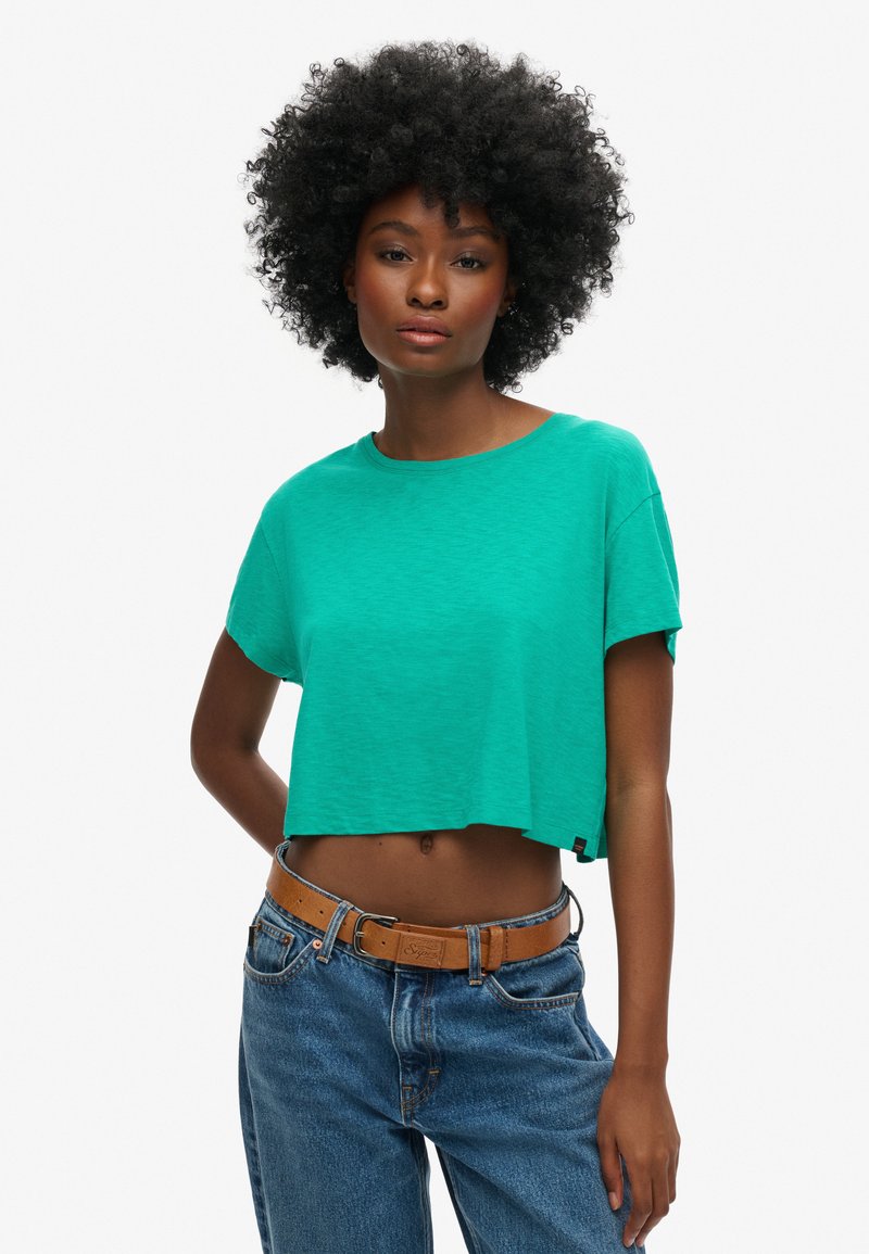 Grøn cropped t-shirt med korte ærmer, lavet af et blødt materiale. Bæres med højtaljede blå jeans og et brunt bælte.