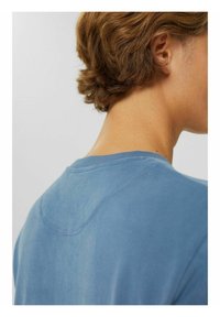 Camiseta de algodón azul con cuello redondo y mangas cortas. Textura suave y variación de color sutil. Detalle de costura expuesta en la parte posterior.