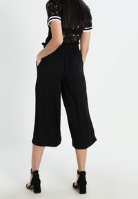 Černé kalhoty culotte s elastickým pasem, bočními kapsami a volným střihem, doplněné černými podpatky pro větší elegantnost.