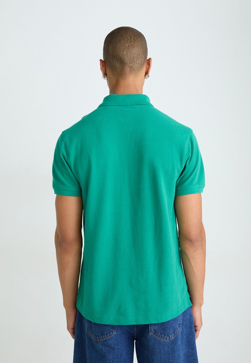 Polo verde con un design semplice, maniche corte e una texture morbida. Presenta un colletto classico e un orlo dritto sul retro.