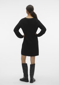 Robe en tricot noire avec des manches longues et des fentes latérales, associée à des bottes en cuir noir jusqu'aux genoux. Silhouette simple et décontractée avec une texture agréable.