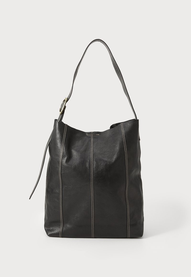 Sac d'épaule en cuir noir avec surpiqûres blanches visibles et boucle réglable sur la sangle, posé contre un fond clair uni.