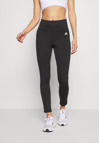 Svarta atletiska leggings med hög midja, slät textur, åtsittande design och diskret vitt logotyp. Dragkedjedetalj längs sidan.