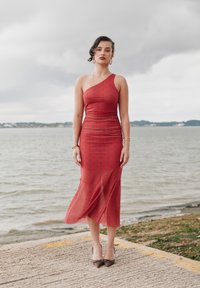 Piros szatén midi ruha egyrészes vállmegoldással, ráncolt textúrával és fekete pöttyökkel. Barna cipővel és karkötőkkel viselve.