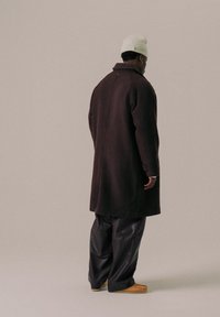 Long dark brown coat with a high collar, featuring a straight cut and smooth texture, paired with loose black leather pants and light-colored shoes.