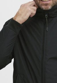 Črna izolirana jakna z visokim ovratnikom, zadrgo in rebrastimi manšeti. Ima gladko teksturo in stranske žepe.