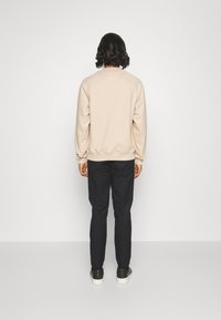 Sudadera beige de manga larga, con puños y dobladillo acanalados, combinada con pantalones de un oscuro azul marino. La vista trasera muestra un diseño simple y limpio, sin patrones.