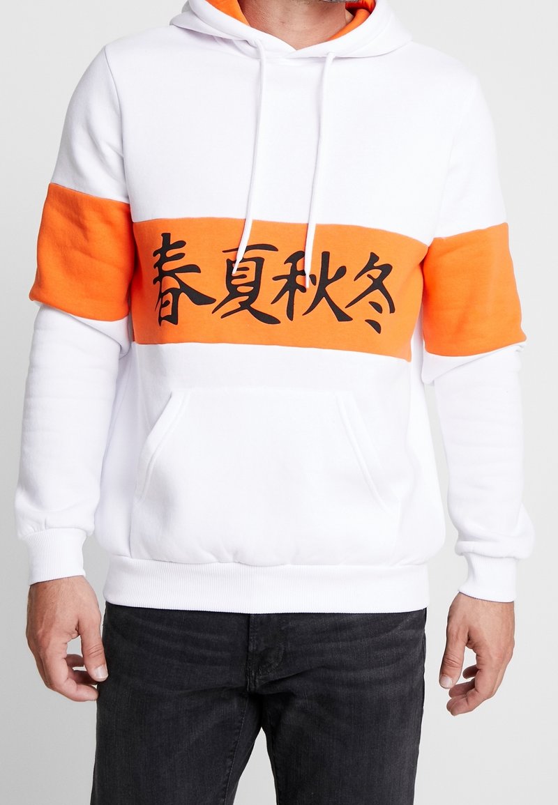 Sweat à capuche blanc avec bande orange portant un texte noir ; fabriqué en tissu doux, comprend une poche avant et une capuche à cordon ajustable.
