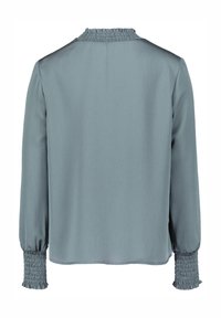 Blouse à manches longues en bleu ardoise doux, dotée d'un col et de poignets smockés avec un tissu texturé et léger. Design épuré avec une coupe décontractée.