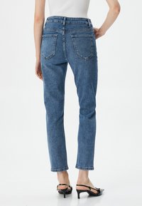 Jeans de mezclilla azul con un diseño de cintura alta y pierna recta. Presenta dos bolsillos traseros y bordes rematados. Combinados con sandalias negras de tacón.