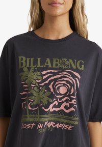 Sort bomuld t-shirt med et grafisk design, der har grøn tekst, pink bølger, palmer og sætningen "Lost in Paradise" nederst.
