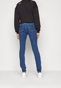 Blå jeans med slim fit, högstretch denim, femfickorsdesign och kontrasterande sömmar. Bärs med en svart sweatshirt och vita sneakers.