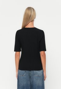 Svart kortermet topp med rund hals og ribbet tekstur, sammen med lyseblå vide jeans, sett bakfra.