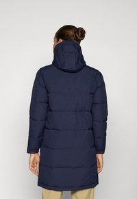 Marineblauwe gewatteerde jas met capuchon, met een gequilt ontwerp, lange mouwen en een middellange snit. Gladde textuur met een moderne silhouet.