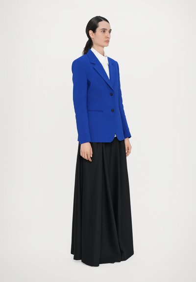 Blue tailored blazer with a notched collar, single-button closure, and two front pockets, paired with a flowing black maxi skirt.