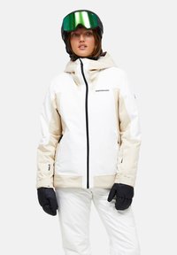 Hvid og beige skijakke med hætte, sorte lynlåse og sorte detaljer. Sammen med sorte handsker og en grøntoneret skihjelm.