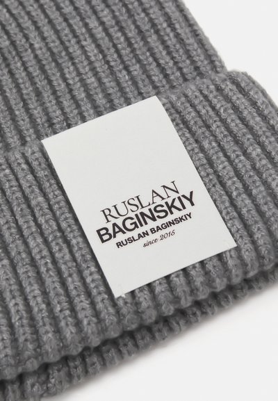 Bonnet en tricot gris avec une texture côtelée. Présente une étiquette tissée affichant "Ruslan Baginskiy" et "depuis 2016" en impression foncée.