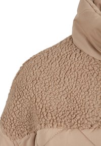Beige Jacke mit weichem, strukturiertem Stoff an den Schultern und glattem Material am Kragen, sowie einem gesteppten Design entlang des Körpers.