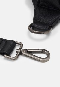 Sangle en cuir noir avec une finition texturée. Comprend des accessoires en métal avec des gravures. Inclut un clip et une boucle pour fixation.