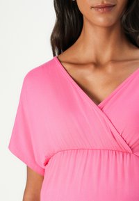 Lett og luftig topp i rosa stoff med V-hals og korte ermer. Har innsnøring i midjen og en glatt, myk tekstur.
