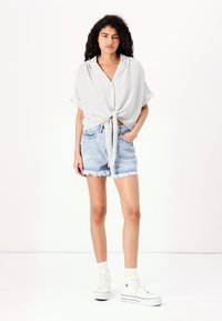 Randig kortärmad skjorta med knut i midjan, i kombination med fransiga denimshorts. Vita hög-top sneakers fulländar outfiten.