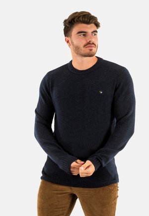 Pull en laine bleu marine avec des manches longues et un col et des poignets côtelés. Présente un petit design brodé sur la poitrine. Texture douce.