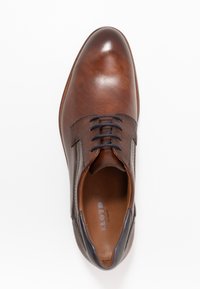 Chaussure en cuir marron avec une finition lisse, des accents texturés et des lacets sombres. Dispose d'un bout arrondi et d'un intérieur rembourré pour le confort.