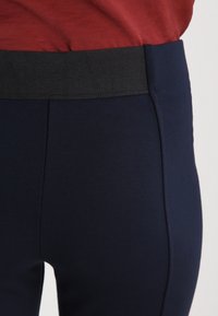 Mörkblå stretchtygsleggings med svart elastisk midja och en mjuk yta. Har en sidokant för en åtsittande design.