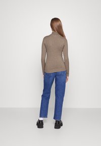 Lichtbruin lange mouwtop met een aansluitende silhouet, gedragen met blauwe denim jeans. De top heeft een subtiele textuur en geribde manchetten.