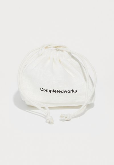 Baltas lino maišelis su raišteliu, ant kurio juodai atspausdintas užrašas "Completedworks". Lygi tekstūra, apvalios formos ir susiraukšlėta viršūnė.