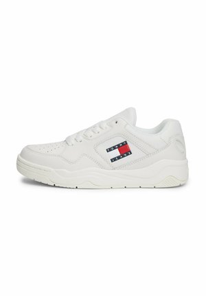 Zapatilla de cuero blanca con puntera perforada, forma redondeada, suela texturizada y un parche de logo en el lateral con colores rojo, blanco y azul.
