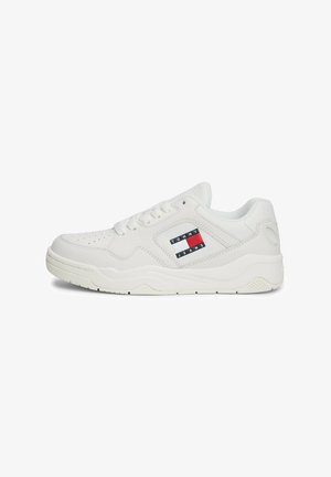 Baskets en cuir blanc avec un bout perforé, forme arrondie, semelle texturée et une étiquette de logo sur le côté avec des couleurs rouge, blanc et bleu.